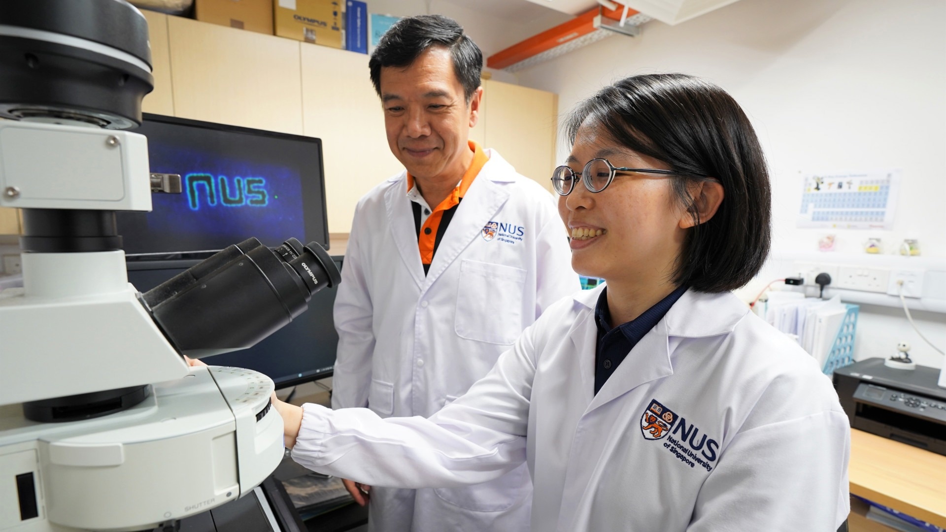 Prof Sow Chorng-Haur (left) and Dr Sharon Lim from the NUS Department of Physics observe a glowing laser-engraved hair under UV light through a microscope.